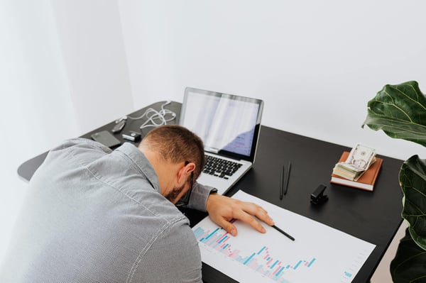 Overworked business owner falling asleep on office desk with laptop and charts, needing a fractional marketing leader